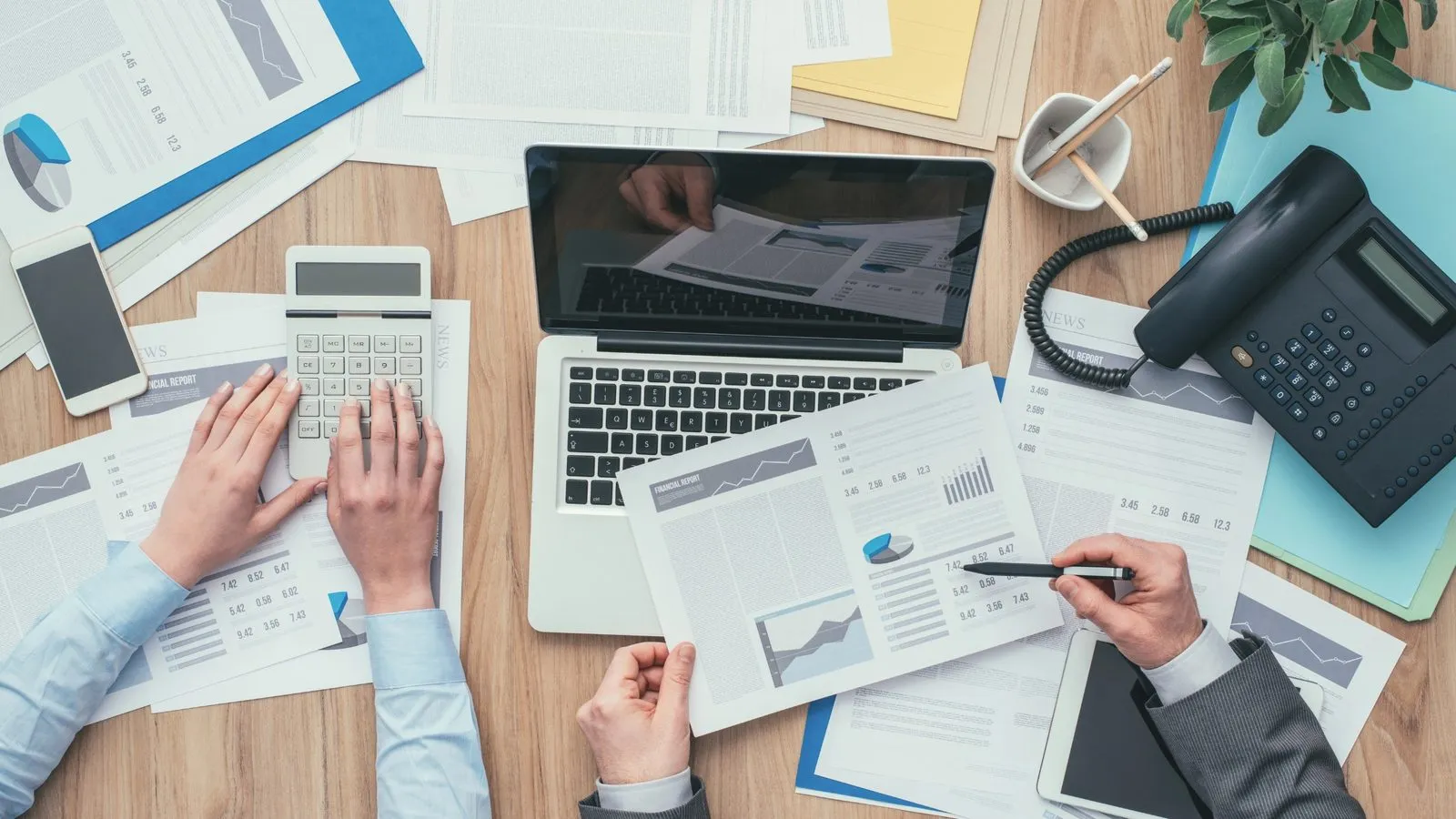 Two people at a desk with a laptop, a calculator and printed financial reports
